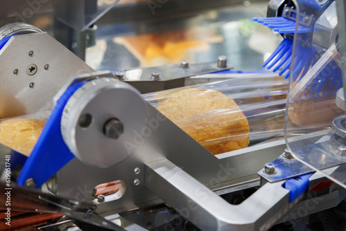 baked bread in food grade plastic bag on conveyor belt moves to seal in packing machine at production line of bakery manufacturing factory. food processing and industry concept.