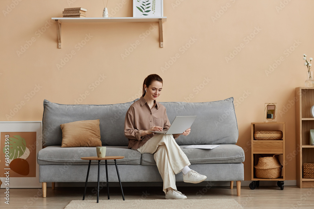 Minimal full length portrait of young elegant businesswoman enjoying work from home and sitting on comfortable sofa reading documents, copy space