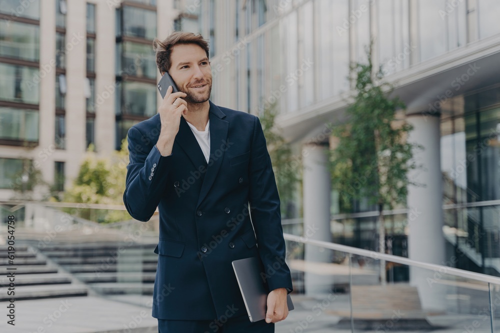 Handsome entrepreneur communicates, uses tech, dressed formal, poses outdoor, solves company issues, collaborates with colleagues