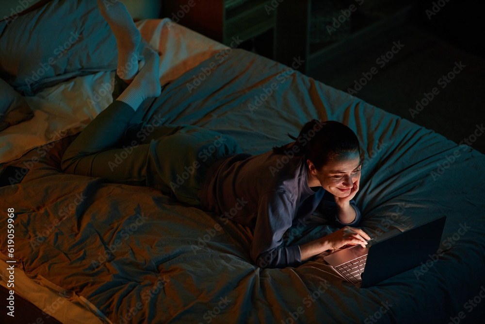 Portrait of young woman watching movies at night while lying on bed