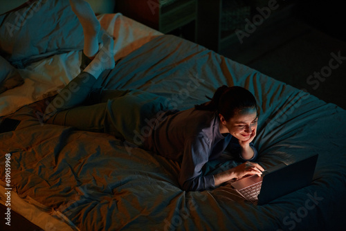 Portrait of young woman watching movies at night while lying on bed