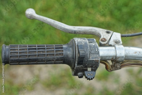 very old cracked rubber throttle stick with a metal lever and part of the steering wheel of a retro non-working motorcycle outdoors during the day