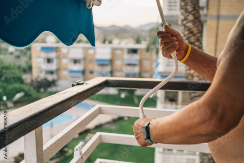 Unrecognizable elderly person closing the awning of his terrace. Hands of unrecognizable man turning the crank to lower the sunshade awning.