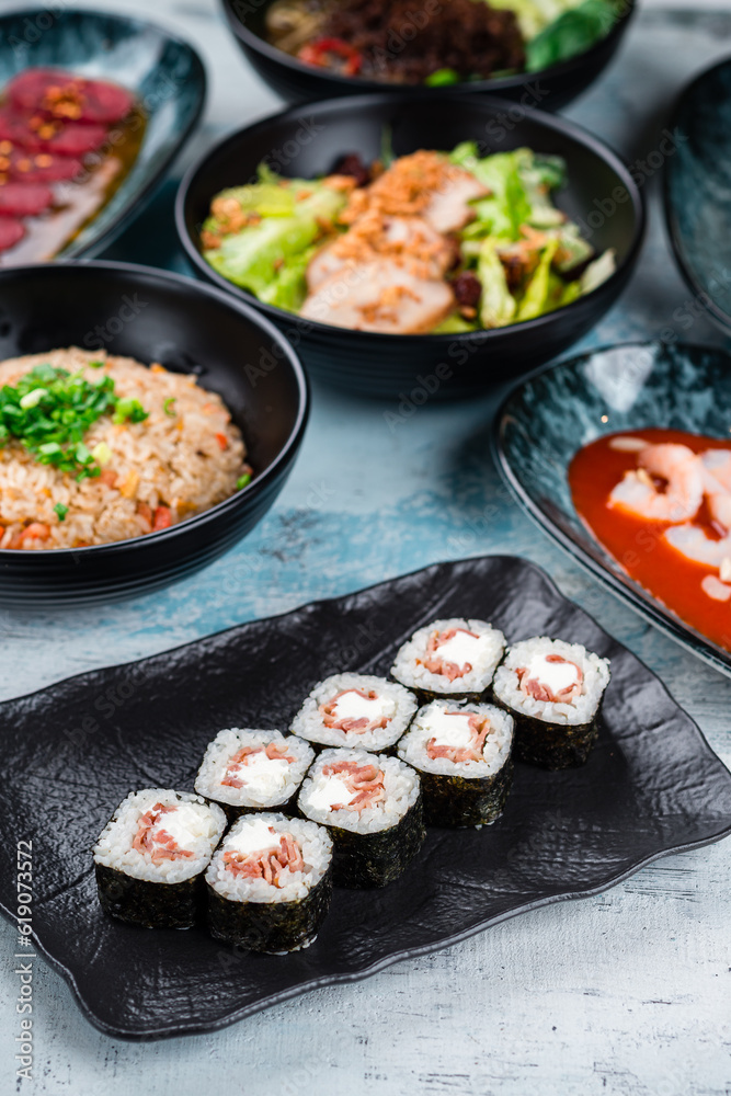 Sushi maki rolls with bacon, salad with chicken fillet and rice with chicken on a table. Sushi maki rolls with bacon, salad with chicken fillet and rice with chicken on a table.