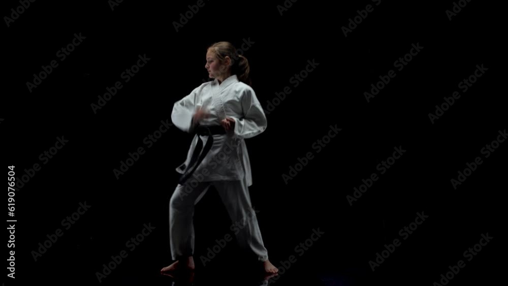 Young girl wearing kimono and practicing karate against black background