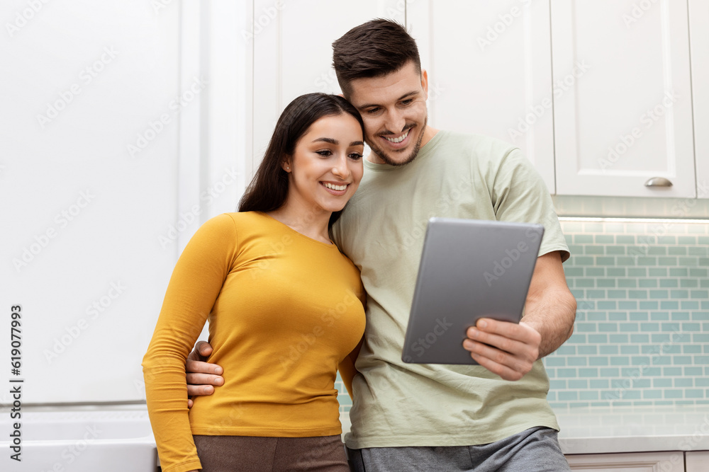 Beautiful young couple taking photo on digital tablet at kitchen Beautiful young couple taking photo on digital tablet at kitchen
