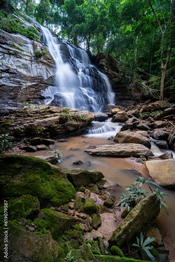 Fototapeta premium Beautiful waterfall in green tropical forest. View of the falling water with splash in rain season know as name Tad Mok, Chiang Mai Thailand. Nature landscape. waterfall in the deep rain forest jungle
