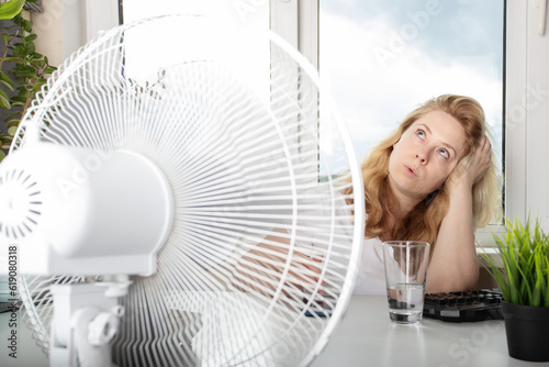 Woman in the office, feeling the refreshing airflow from a fan, summer heatwave
