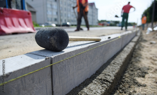 Concrete curbs are installed along the road, a hammer is on top.