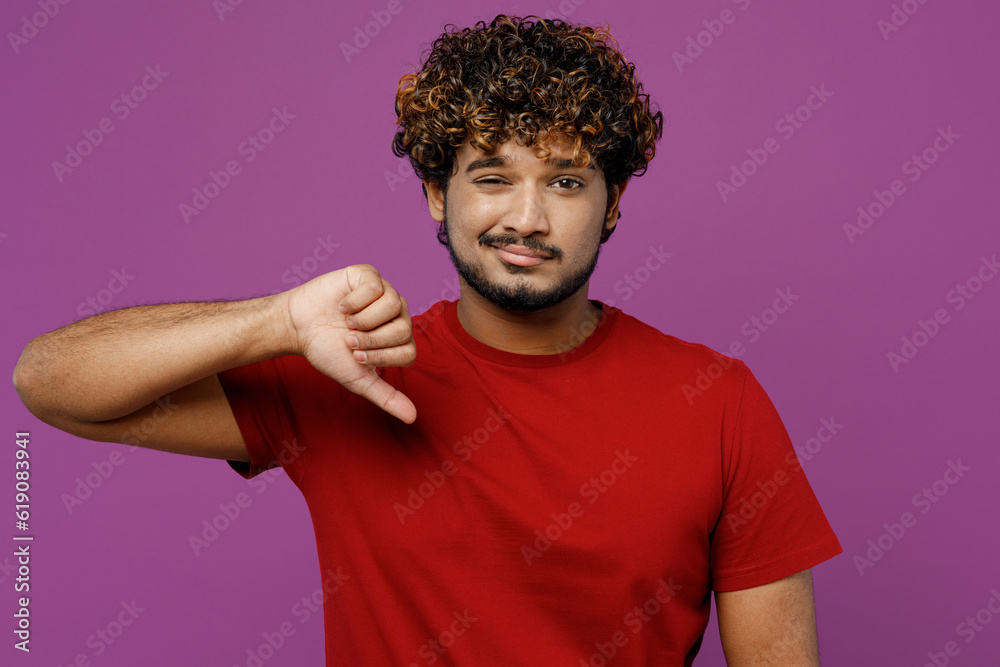 Young dissatisfied displeased sad Indian man he wear red t-shirt casual clothes showing thumb down dislike gesture look camera isolated on plain purple background studio portrait. Lifestyle concept. Young dissatisfied displeased sad Indian man he wear red t-shirt casual clothes showing thumb down dislike gesture look camera isolated on plain purple background studio portrait. Lifestyle concept.