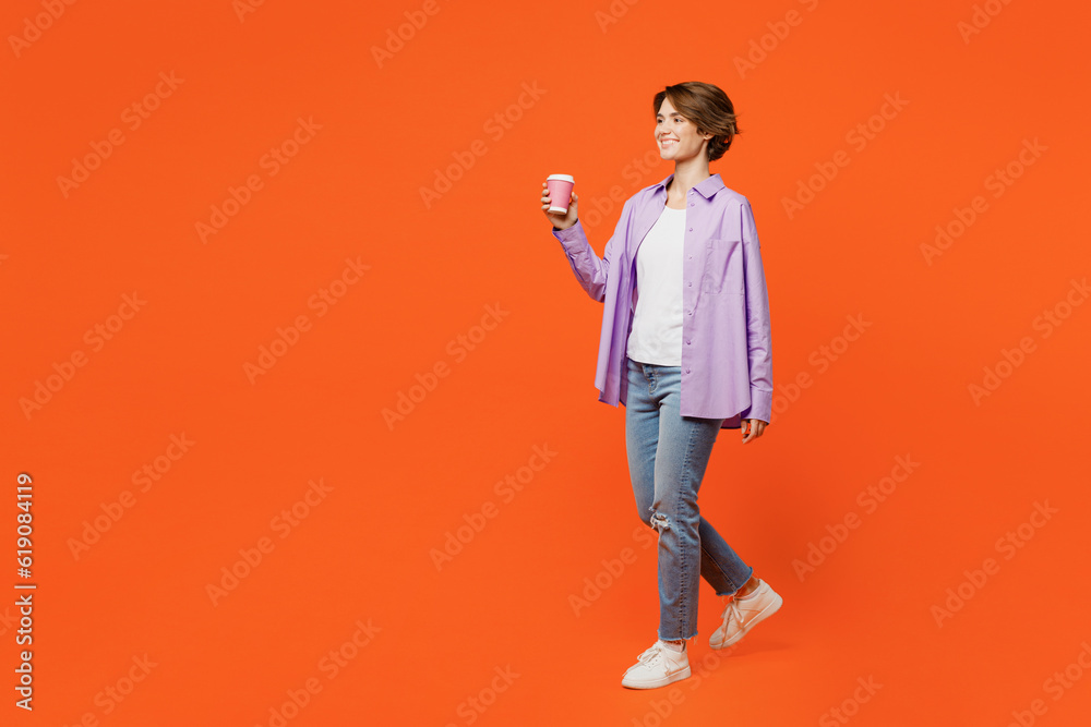 Full body young woman wear purple shirt white t-shirt casual clothes hold takeaway delivery craft paper brown cup coffee to go isolated on plain orange background studio portrait. Lifestyle concept. Full body young woman wear purple shirt white t-shirt casual clothes hold takeaway delivery craft paper brown cup coffee to go isolated on plain orange background studio portrait. Lifestyle concept.