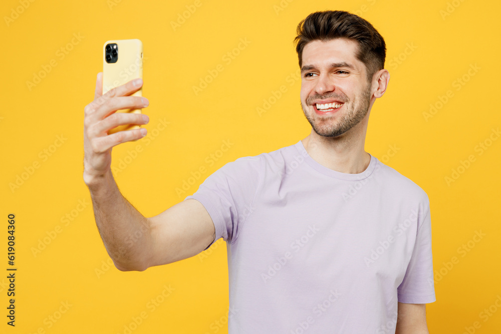 Young smiling man he wear light purple t-shirt casual clothes doing selfie shot on mobile cell phone post photo on social network isolated on plain yellow background studio portrait Lifestyle concept Young smiling man he wear light purple t-shirt casual clothes doing selfie shot on mobile cell phone post photo on social network isolated on plain yellow background studio portrait Lifestyle concept