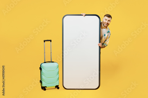 Traveler man wearing casual clothes hold suitcase big huge blank screen mobile cell phone isolated on plain yellow background Tourist travel in free spare time rest getaway. Air flight trip concept. #619084341