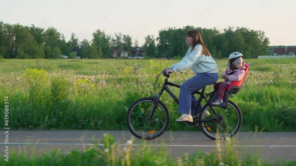 A woman riding a bicycle with a 3-year-old daughter on a rural road A woman riding a bicycle with a 3-year-old daughter on a rural road
