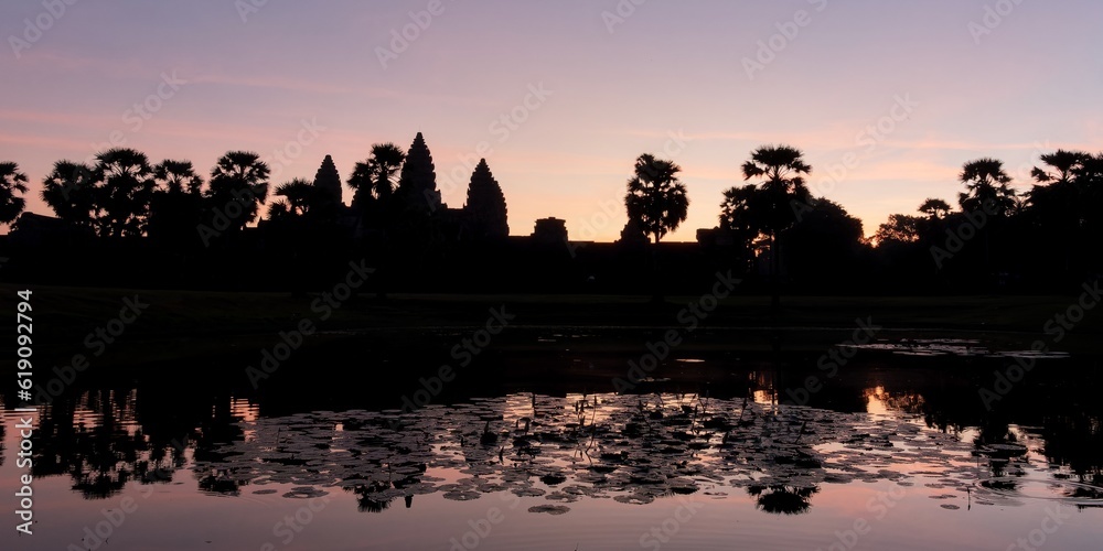 A serene view of the Angkor Temple and its environs at dusk, with the shadows creating a captivating outline in the Cambodian landscape.