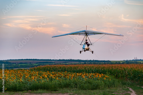 White motorized hang glider flies above sunflower field