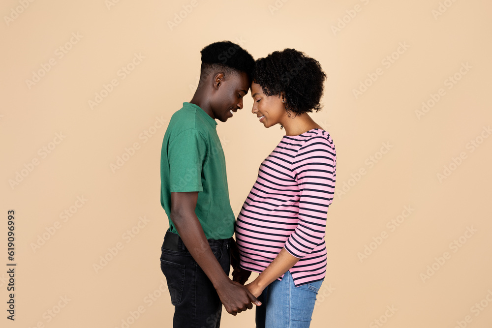 Glad young african american husband holding hands of pregnant wife with big belly in casual Glad young african american husband holding hands of pregnant wife with big belly in casual