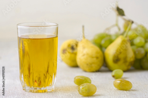 Juice of pears and grapes in a glass on a white wooden background
