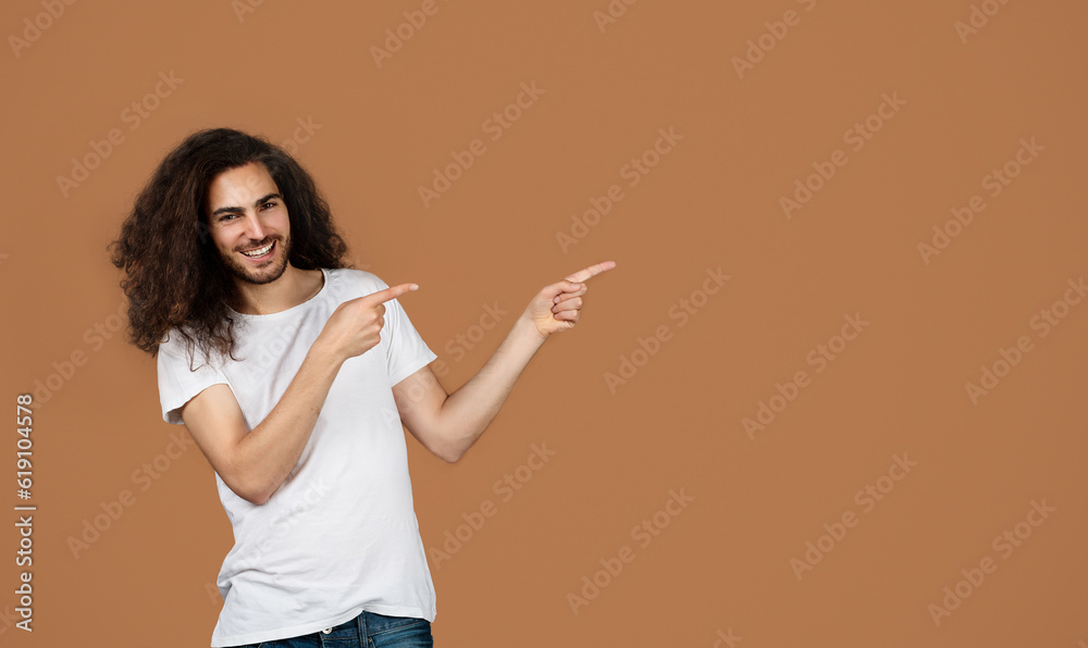 Happy Middle Eastern Young Man Pointing Fingers Aside, Brown Background Happy Middle Eastern Young Man Pointing Fingers Aside, Brown Background