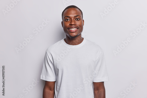 Horizontal shot of handsome smiling dark skinned man poses for making photo happy to have day off wears casual t shirt isolated over white background. People ethnicity and happy emotions concept