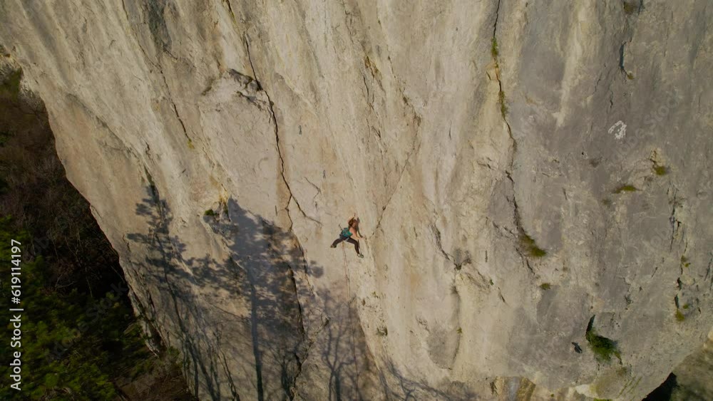 AERIAL: Agile young lady lead climbing a difficult route in broad limestone cliff. She uses chalk for a better grip. Magnificent drone view of an incredible climbing playground in Karst landscape. AERIAL: Agile young lady lead climbing a difficult route in broad limestone cliff. She uses chalk for a better grip. Magnificent drone view of an incredible climbing playground in Karst landscape.