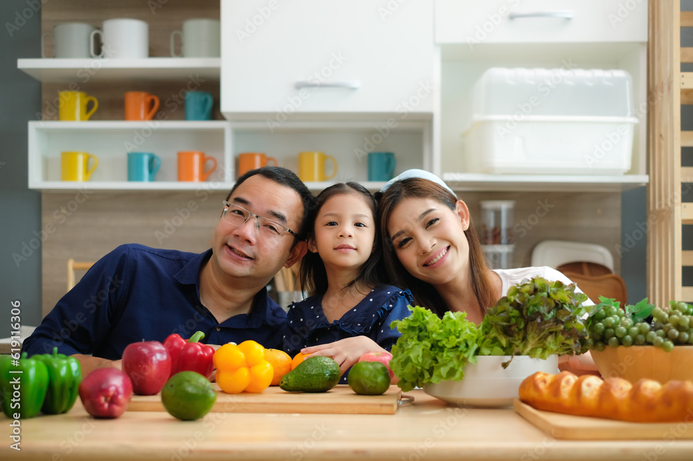 Cute little girl with mother and father with vegetables and ingredients laying on table for cooking in the kitchen.