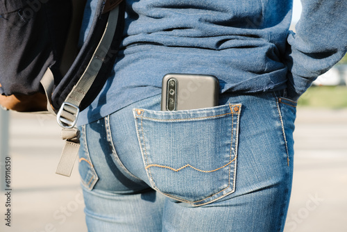 Smartphone sticks out of the back pocket of jeans. The woman put her cell phone in the back pocket of her jeans. The concept of pickpocketing, indiscretion, frivolity.