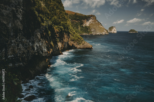 Rock ocean shore timelapse aerial viea with dramatic crashing waves at cliff in Indonesia, Nusa Penida Island. Epic nobody nature scape at sea bay water under cloudy sky. Cinematic shot