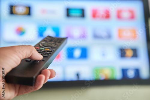 Multimedia streaming concept. Hand holding remote control. TV screen with lot of pictures.