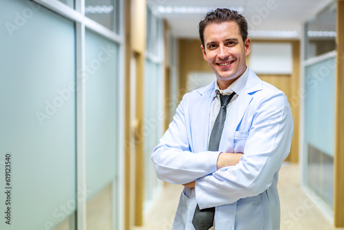 Sincere smile. Portrait of handsome male doctor wearing white coat standing In hospital corridor keeping smile on face and looking straight at camera.