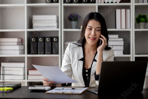 Beautiful asian woman talking on the phone, businesswoman working in office attentively to grow and modernize start-up business, she is analyzing company's market and financial data. © kamiphotos