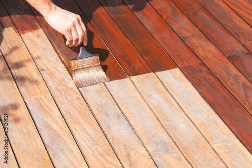 Leinwand Poster Ipe wood worker's hand is oiling terrace decking with a painting brush