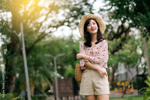 Portrait of asian young woman traveler with weaving hat and basket happy smile on green public park nature background. Journey trip lifestyle, world travel explorer or Asia summer tourism concept.