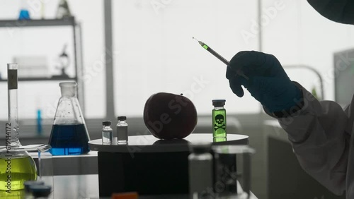Dark silhouette of a male scientist with a syringe. A researcher injects pesticides and nitrates into a red apple with a syringe. GMO concept and genetically modified organism. HDR BT2020 HLG Material
