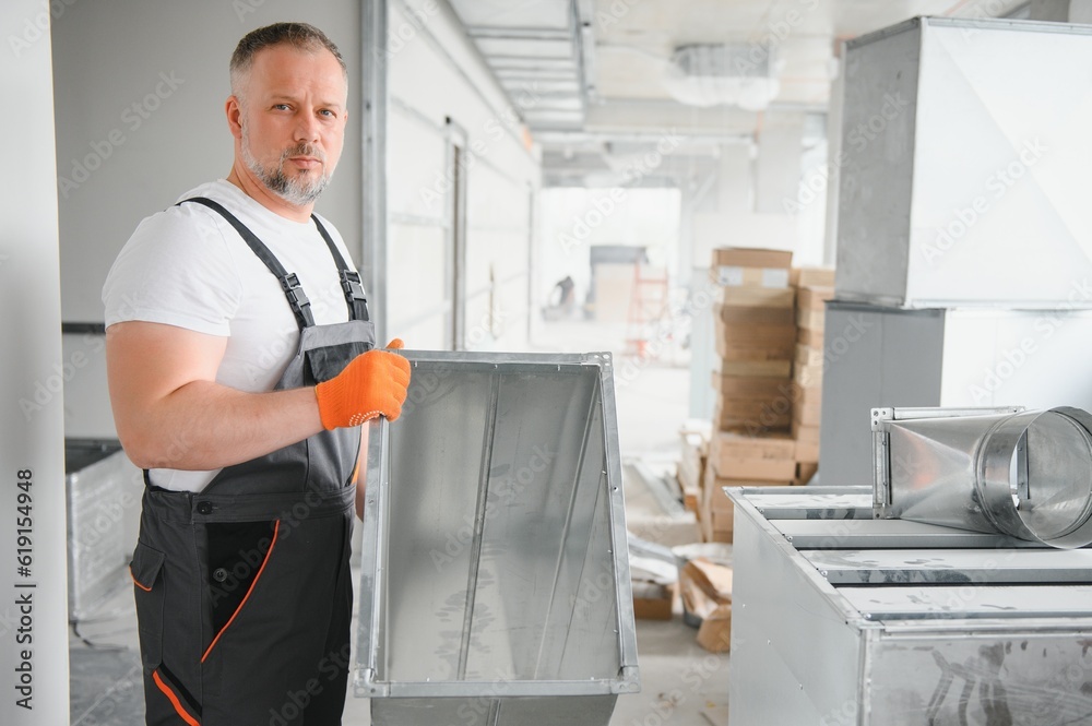 Man setting up ventilation system indoors. A male worker installs air ventilation pipes in a new office building. Man setting up ventilation system indoors. A male worker installs air ventilation pipes in a new office building.