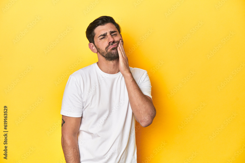 Caucasian man in white t-shirt on yellow studio background having a strong teeth pain, molar ache. Caucasian man in white t-shirt on yellow studio background having a strong teeth pain, molar ache.