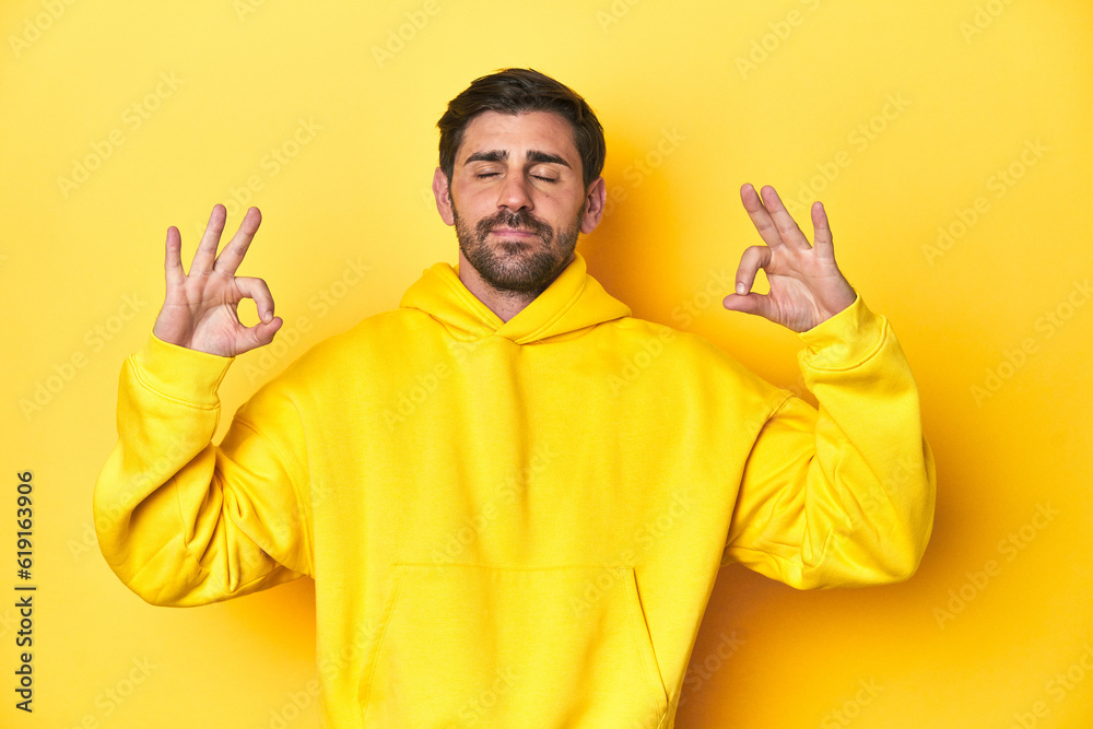 Man in yellow hoodie, monochrome studio backdrop relaxes after hard working day, she is performing yoga.