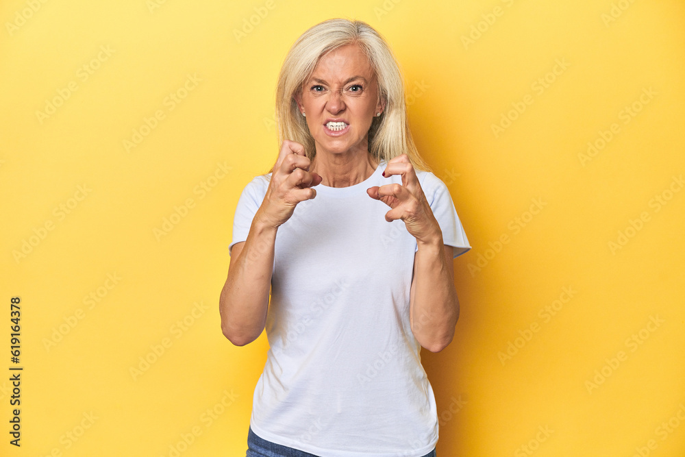 Middle-aged Caucasian woman in white t-shirt, yellow studio upset screaming with tense hands. Middle-aged Caucasian woman in white t-shirt, yellow studio upset screaming with tense hands.