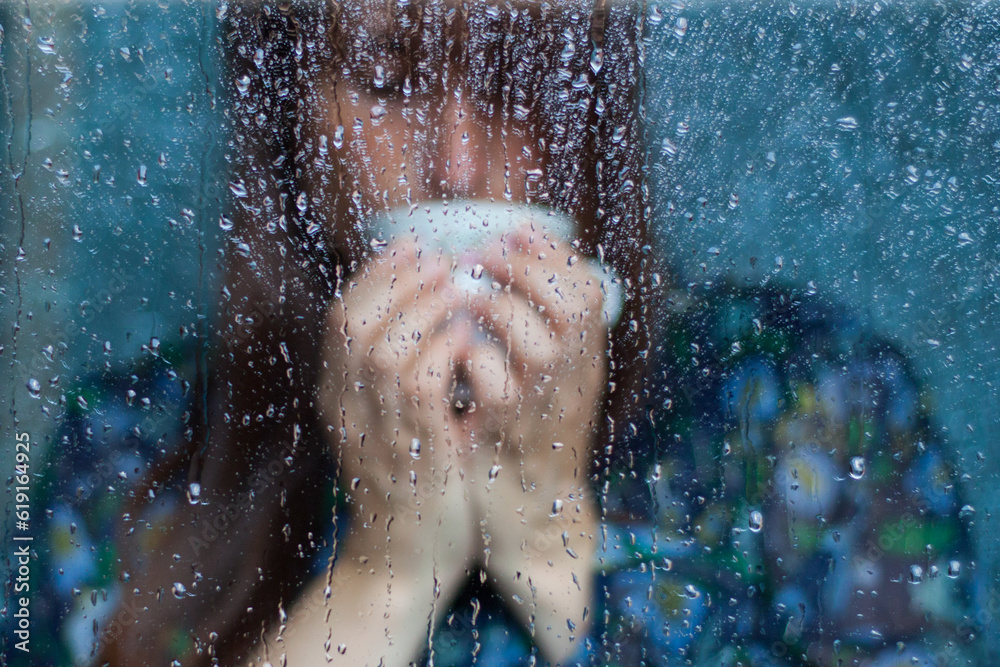 Fototapeta premium mujer bebiendo de una taza de café detrás de cristal con gotas con vestido azul