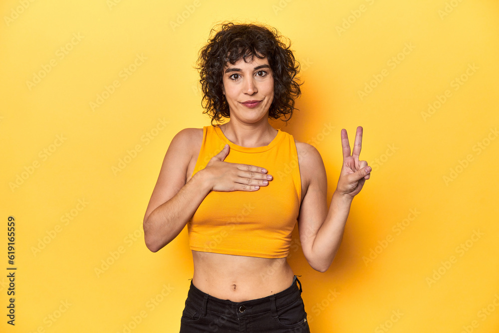 Curly-haired Caucasian woman in yellow top taking an oath, putting hand on chest. Curly-haired Caucasian woman in yellow top taking an oath, putting hand on chest.