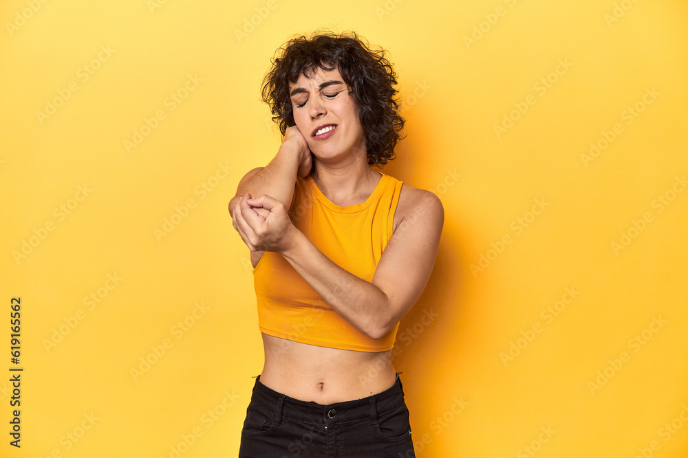 Curly-haired Caucasian woman in yellow top massaging elbow, suffering after a bad movement. Curly-haired Caucasian woman in yellow top massaging elbow, suffering after a bad movement.