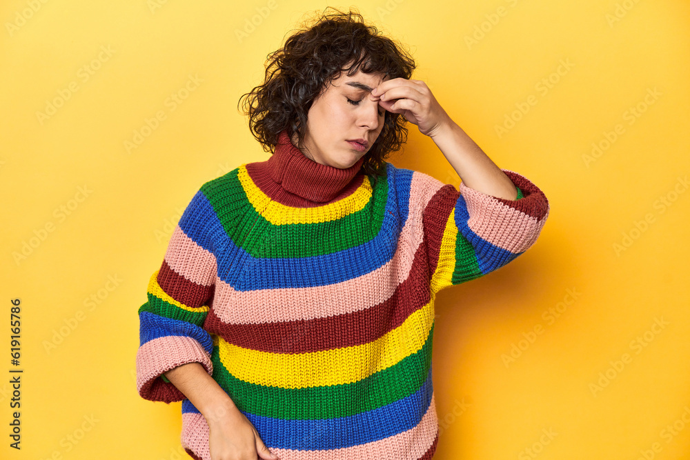 Curly-haired woman in multicolor sweatshirt having a head ache, touching front of the face. Curly-haired woman in multicolor sweatshirt having a head ache, touching front of the face.