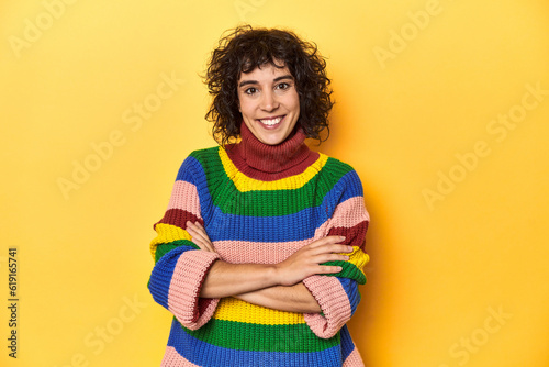 Curly-haired woman in multicolor sweatshirt who feels confident, crossing arms with determination.