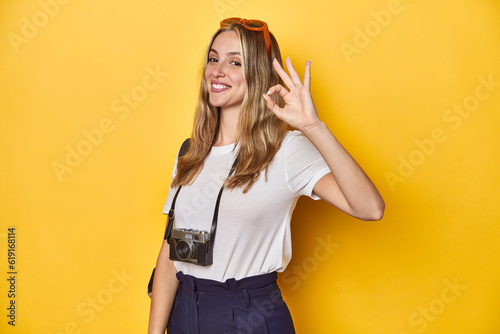 Young Caucasian traveler with vintage camera on yellow backdrop, Young Caucasian traveler with vintage camera on yellow backdropcheerful and confident showing ok gesture.