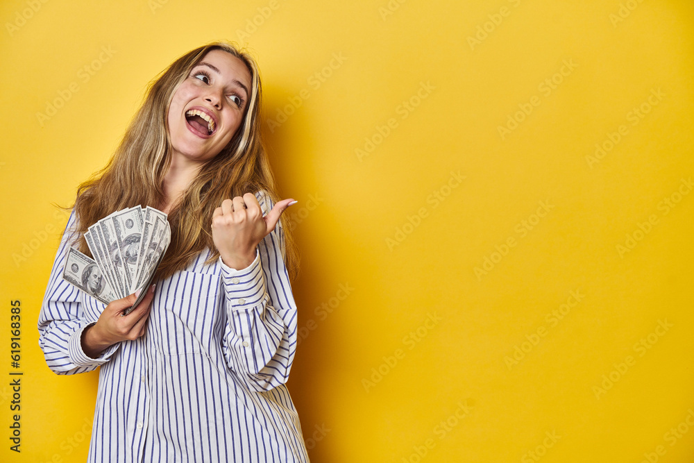 Young Caucasian Woman Holding Cash points with thumb finger away, laughing and carefree. Young Caucasian Woman Holding Cash points with thumb finger away, laughing and carefree.