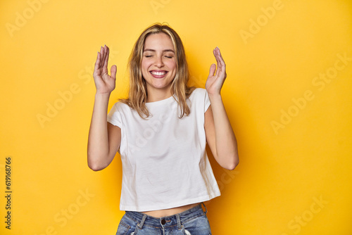 Young blonde Caucasian woman in a white t-shirt on a yellow studio background, joyful laughing a lot. Happiness concept.