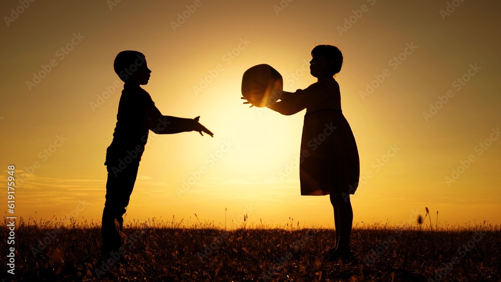 Children play with big ball in park against backdrop of sun. Happy
