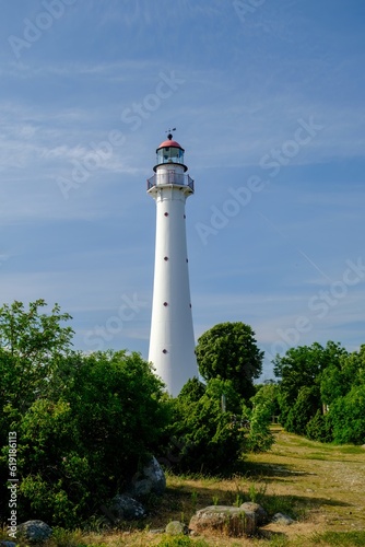 Kihnu island lighthouse in Estonia. Stand alone single white lighthouse stones green forest summer blue sky photo