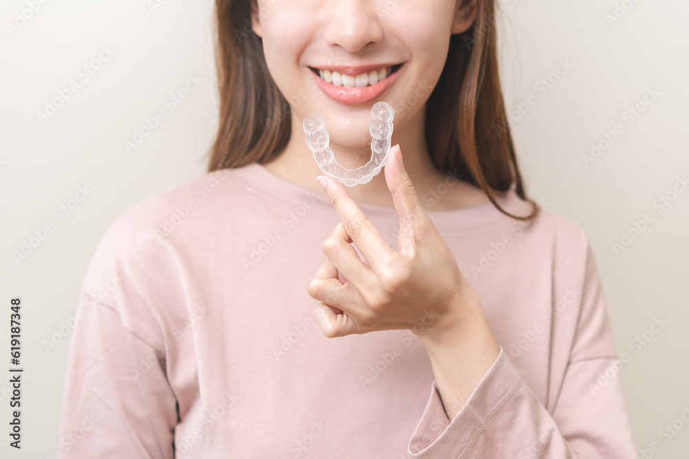 © KMPZZZ - Dental invisible braces, beautiful smiling asian young woman holding invisalign braces, wearing orthodontic silicone trainer, white smile using invisible whitening tray. Stomatology, dental healthcare © KMPZZZ - Dental invisible braces, beautiful smiling asian young woman holding invisalign braces, wearing orthodontic silicone trainer, white smile using invisible whitening tray. Stomatology, dental healthcare