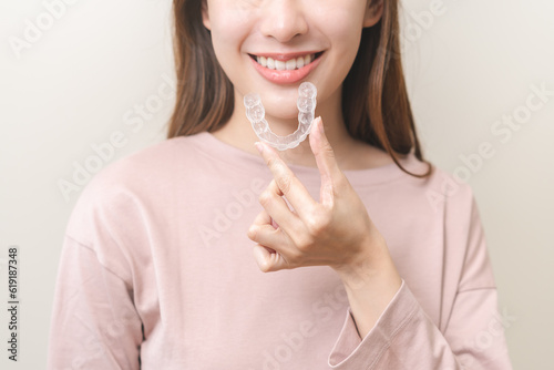 Dental invisible braces, beautiful smiling asian young woman holding invisalign braces, wearing orthodontic silicone trainer, white smile using invisible whitening tray. Stomatology, dental healthcare photo